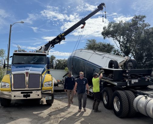 Tow truck and crane positioning a large vessel in the Maverick Marine Service's boat yard for demolition and disposal